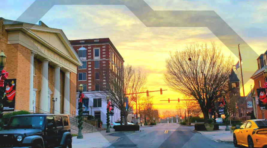 View of street in Rock Hill, SC at sunset with a jeep parked on the side of the road and several building in sight.